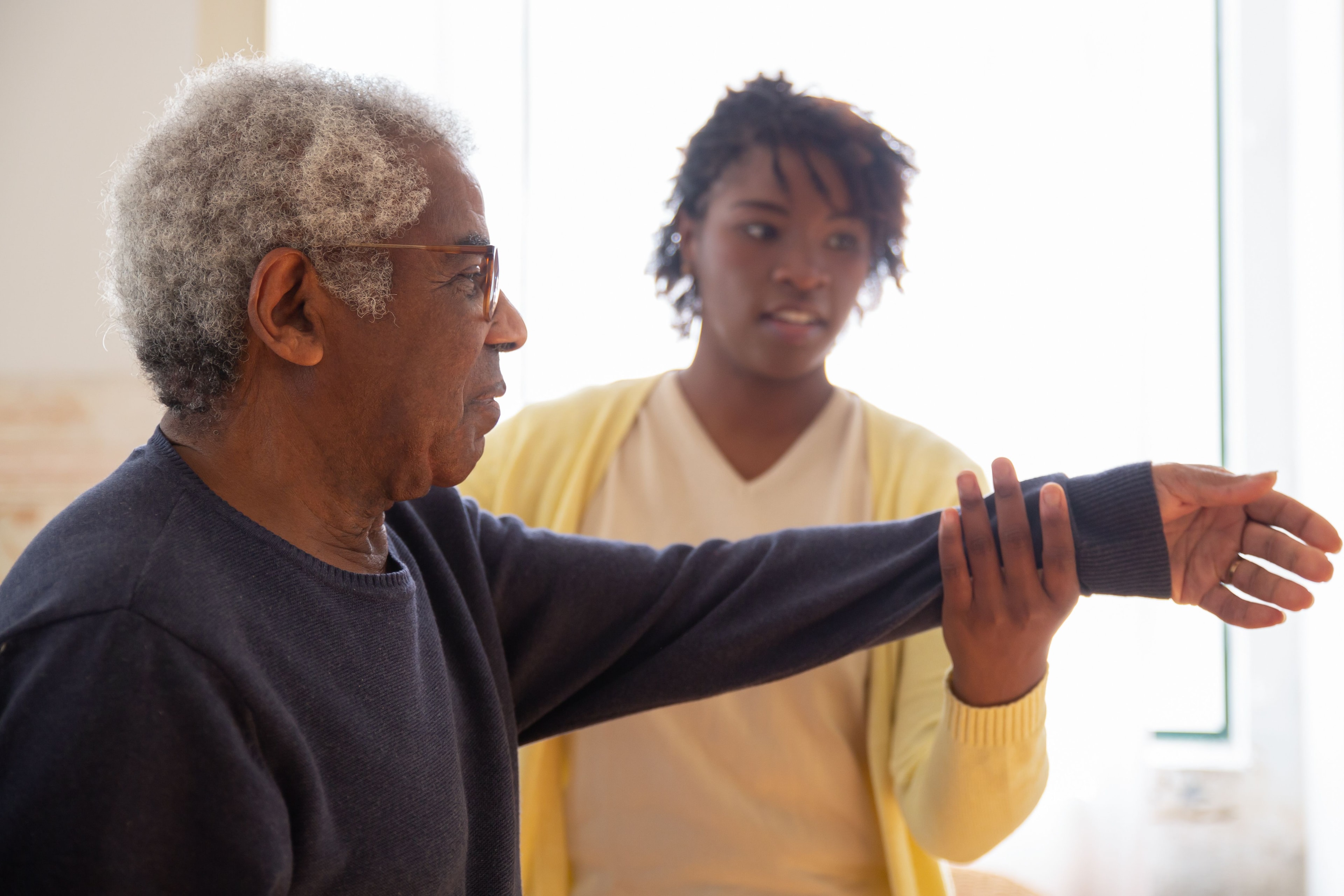 Senior man demonstrating arm exercise with caregiver during in-home care session